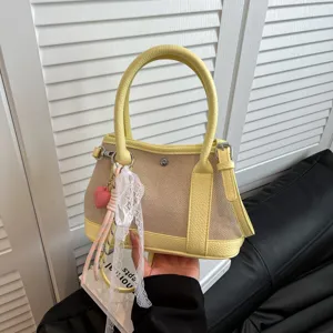 Bolso de mano amarillo de lona y malla con detalles de cuero, asa superior y cinta.