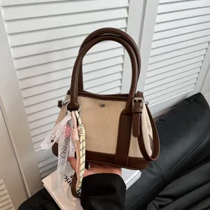 Detalle de bolso de lona y piel, elegante bolso beige y marrón con colgante de encaje chic.