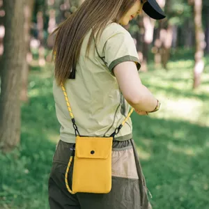 Vista dettagliata di una mini borsa a tracolla gialla per telefono indossata in un parco.