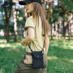 Dettaglio di una mini borsa a tracolla nera per cellulare con tracolla intrecciata e bottone.