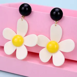 Primer plano detalle elegante pendientes acrílicos bola negra flores blancas fondo rosa.
