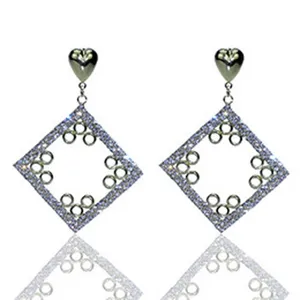 Primer plano detalle de pendientes geometricos de rombo de pedreria con corazon superior.