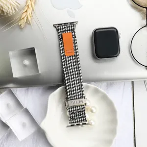 Detailed view of the black and white houndstooth canvas watch band with orange pull tab.
