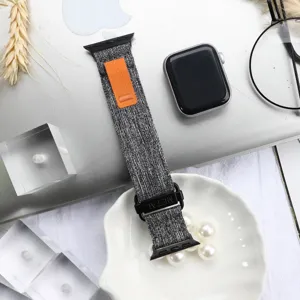 Nylon canvas loop watch strap detail, grey band with orange pull tab and metal buckle.