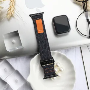 Detailed view of canvas watch strap loop with metal buckle and orange accent in flat lay setup.