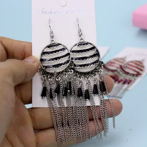 Primer plano detallado de pendientes colgantes geométricos vintage con borlas negras y cadenas.