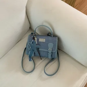 Bella vista di dettaglio della borsa in denim blu con targhetta metallica e ciondolo.