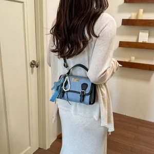 Borsa a mano da donna in denim blu elegante con finiture in pelle nera e ciondolo di perle.