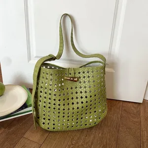 Dettaglio borsa a spalla in pelle intrecciata verde, motivo traforato con fibbia in corno.
