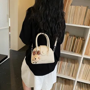 Vista dettagliata di una borsa a tracolla a conchiglia beige chic con ciondolo orsetto.