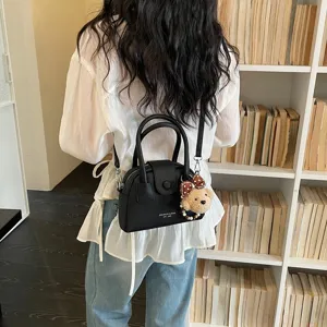 Vista dettagliata della borsa a tracolla nera a conchiglia con ciondolo orsetto, accessorio elegante.