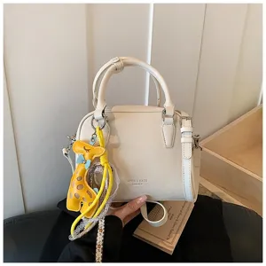 Chic white crossbody handbag with cute yellow giraffe pendant, premium leather style for women.