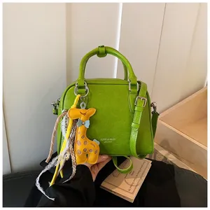 Green leather handbag detail showcasing yellow giraffe charm, lace ribbon, and sturdy top handle.