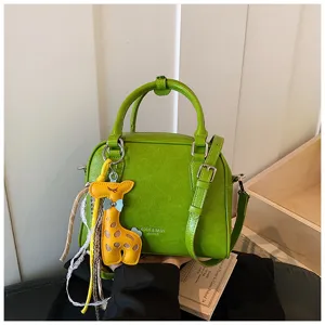 Detail shot of the green leather crossbody bag featuring a cute yellow giraffe pendant.