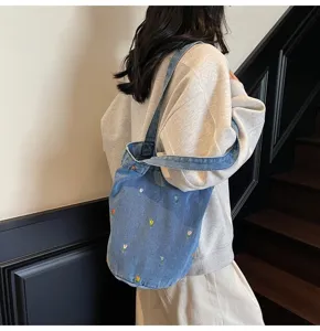 Vue détaillée d'un sac seau en denim bleu avec broderie de tulipes mignonnes porté par modèle.