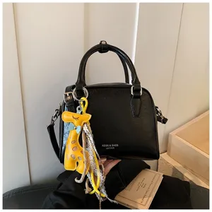 Black leather shoulder bag detail with cute yellow giraffe charm and lace ribbon decoration.