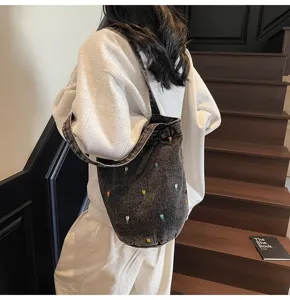 Vue détaillée du sac seau en denim gris foncé avec broderie de tulipes colorées et bandoulière.