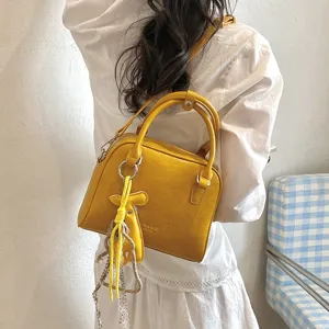 Detailed view of yellow shoulder cross-body bag with stylish pendant and double handles.