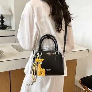 Detail shot of chic black patent leather shoulder bag with cute giraffe charm and scarf.