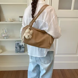 Detalle de bolso de hombro de cuero suave con colgante de osito y textura litchi.