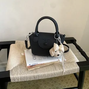 Dettaglio di una borsa in pelle nera con manico superiore e grazioso ciondolo in peluche.