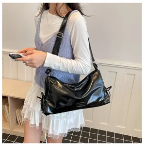 Gros plan d'un sac à épaule coussin élégant en cuir verni noir porté par un modèle.