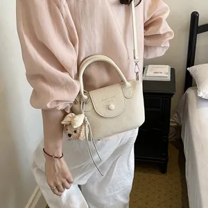 Vista dettagliata della borsa a tracolla beige minimalista con ciondolo cucciolo di peluche.