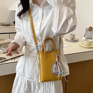 Detail view of stylish yellow crossbody phone bag with chic keychain charm in modern cafe scene.