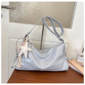 Gros plan du sac porté épaule souple gris clair avec pendentif étoile sur bureau en bois.