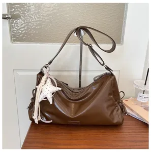 Détail du sac porté épaule marron brillant, pendentif étoile en peluche, style sac oreiller.