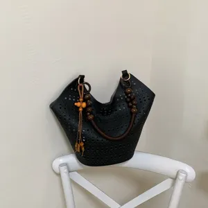 Detailaufnahme der schwarzen Lasercut Schultertasche mit schicken Holperlen-Griffen.