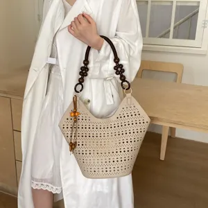 Detailansicht der beigen Lochmuster-Tasche mit Perlenhenkel und Holzquaste im Alltag.