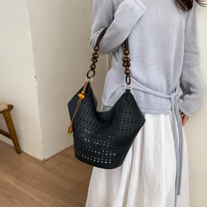Detailansicht einer schwarzen, geflochtenen Schultertasche mit Holzperlen-Griff im Sommer.