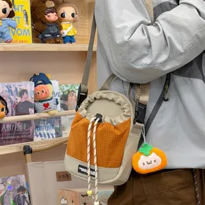 Casual canvas crossbody bag with contrast color design, drawstring closure, and cute plush charm.