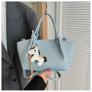 Vue détaillée du sac seau élégant en cuir bleu clair avec nœuds chics et charmant pendentif cheval.