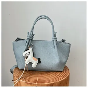 Gros plan sur le sac à main en cuir bleu clair avec anses nouées et charmant pendentif.