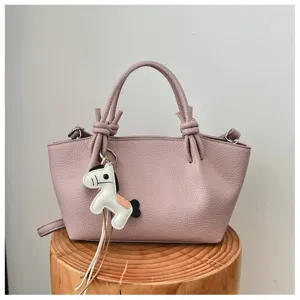 Gros plan d'un sac à main élégant en cuir rose avec poignées nouées et charm cheval en cuir.