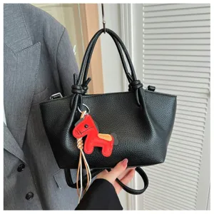 Sac à épaule en cuir texturé noir avec pendentif cheval rouge et poignées nouées.