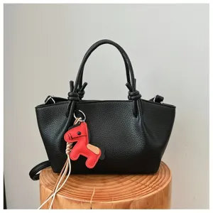 Sac à main en cuir texturé noir avec poignées nouées élégantes et charm de cheval rouge.