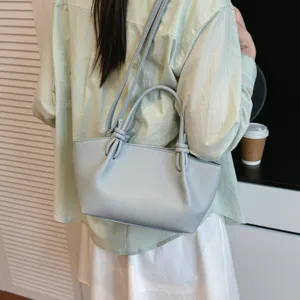 Vue détaillée du sac à bandoulière en cuir texturé gris clair avec poignées nouées élégantes.