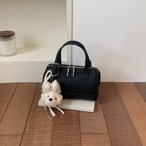 Detailed view of the black textured leather boston bag with a cute plush puppy charm.