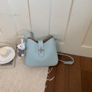 Minimalistische hellblaue Leder Eimer Tasche mit Metallverschluss und Plüsch Anhänger.