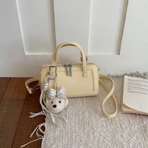 Detailed view of trendy yellow small pillow shoulder bag with cute bow bear pendant.