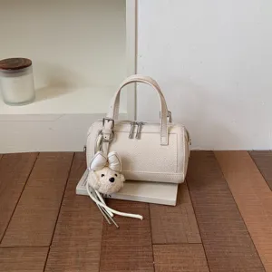 Chic beige leather pillow bag with cute plush bear charm, perfect for daily commuting.