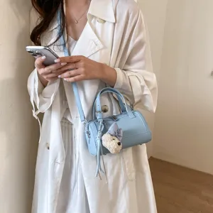 Detail shot of a light blue cylindrical shoulder bag with a cute plush dog charm accessory.