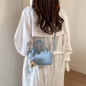 Detailed shot of light blue cylindrical crossbody pillow bag with cute bear pendant.