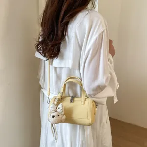 Close-up view of the yellow mini pillow shoulder bag with cute plush pendant and metal zipper detail.
