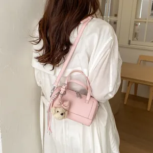 Chic pink shoulder pillow bag with cute plush bear charm, perfect for daily fashion commuting.