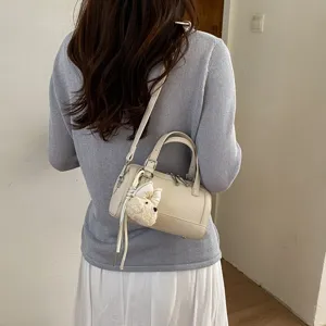 Detailed view of trendy chic cylindrical shoulder crossbody pillow bag with dog charm.