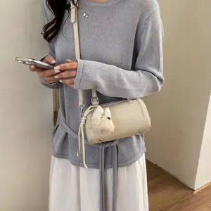 Close up of chic beige leather cylindrical pillow crossbody bag with cute plush pendant.